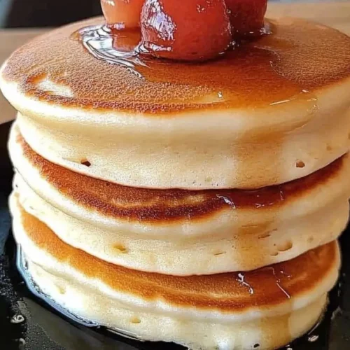 Stack of thick, fluffy Japanese soufflé pancakes drizzled with syrup and topped with glazed cherries on a black plate